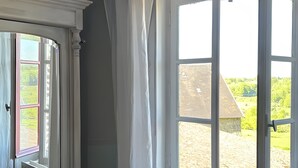 Een kamer met een bed, een radiator, een raam met gordijnen en uitzicht op de omgeving.