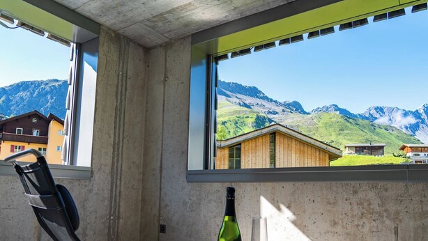 Une chambre avec vue sur les montagnes, une bouteille de vin et un verre sur une table.