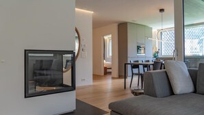 Un salon moderne avec un canapé, une cheminée, un coin repas comprenant une table et des chaises, et une cuisine en arrière-plan.