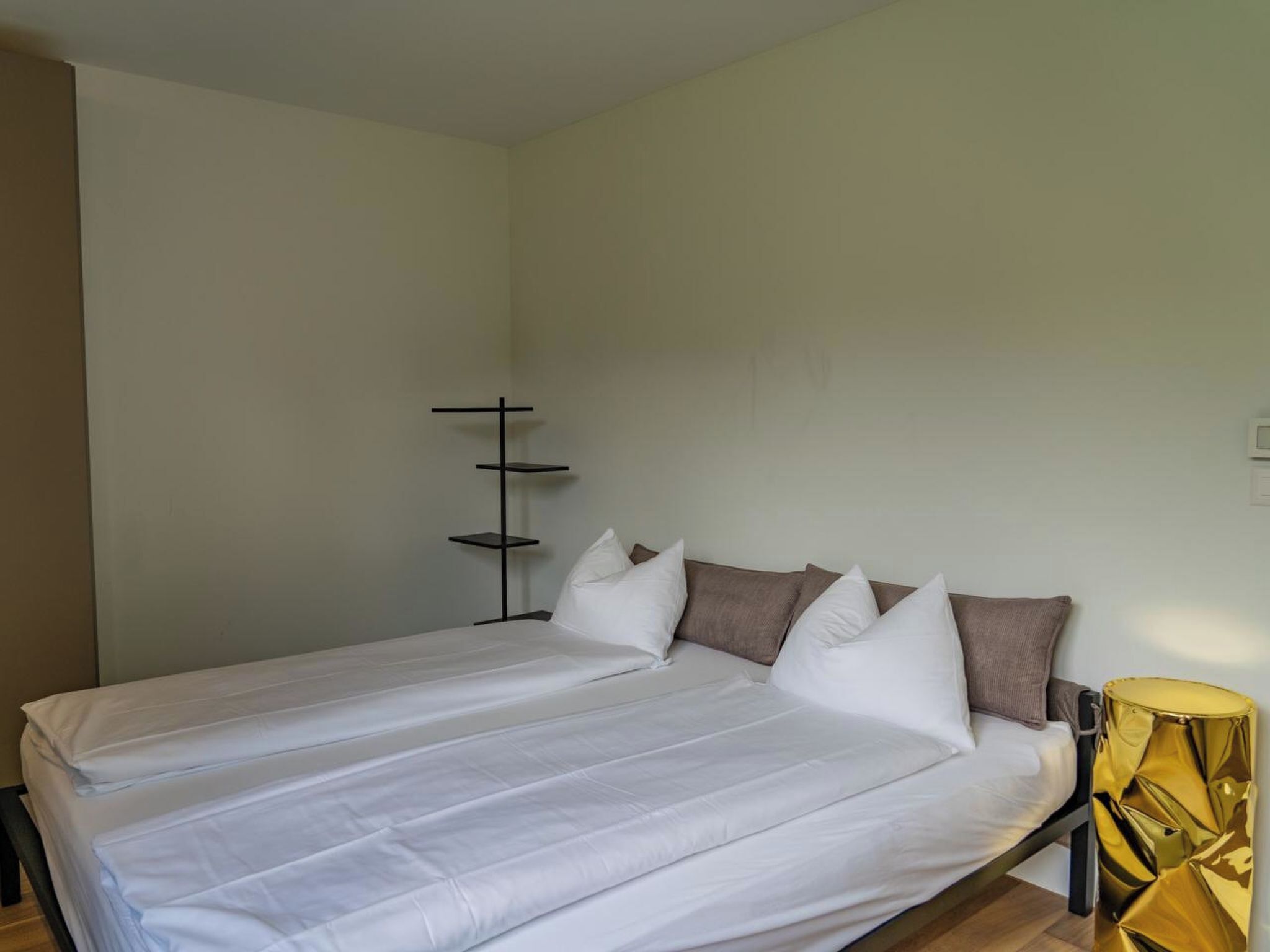 A single bed with white bedding, a black bedside table, and a gold-colored decorative item.