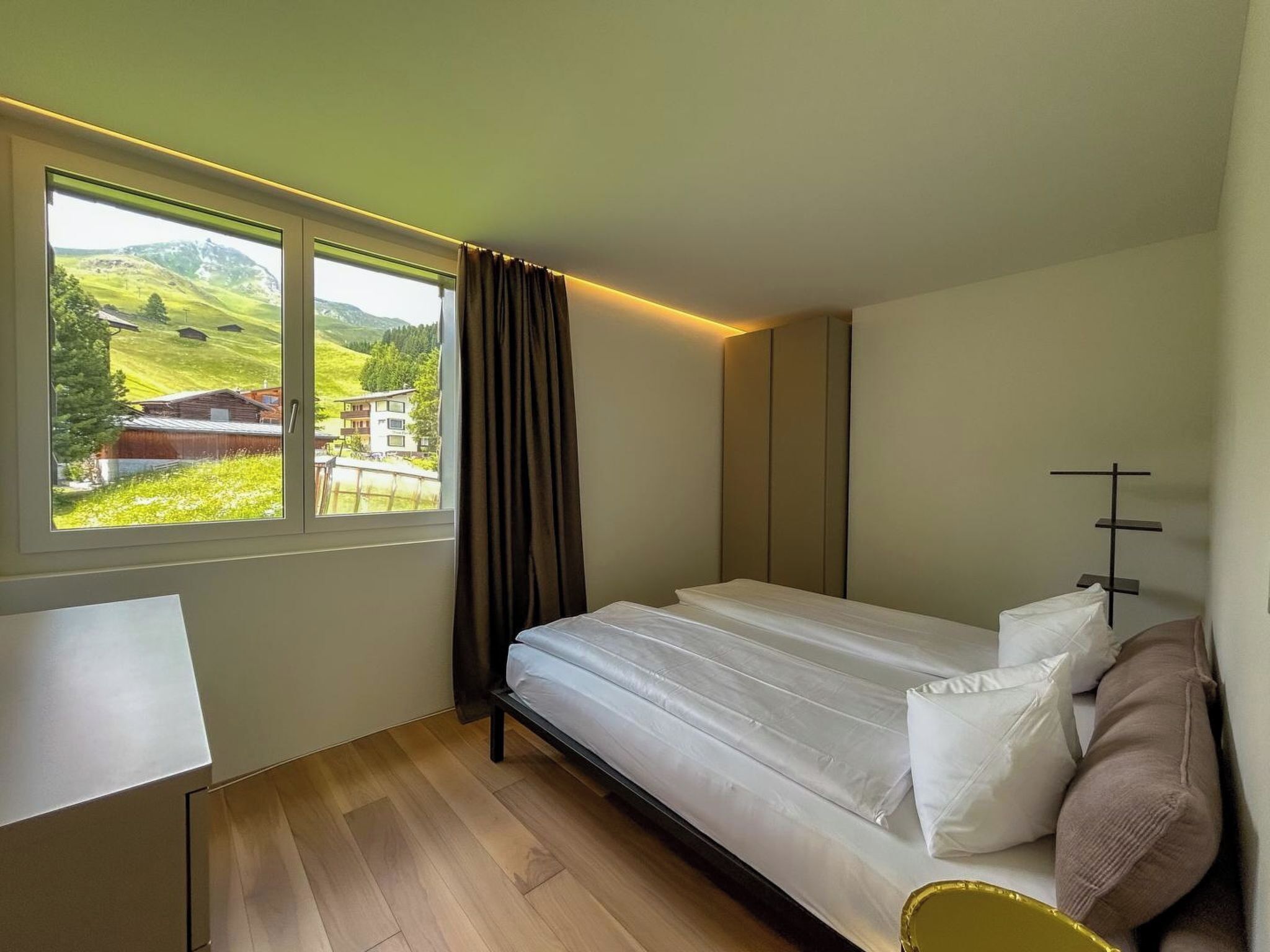 A bedroom with a bed, a window with curtains, a bedside table, and a view of a green landscape.