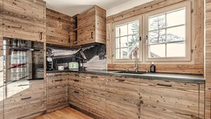 Een keuken met houten kastjes, een ingebouwde kookplaat en een raam met uitzicht op een besneeerd landschap.