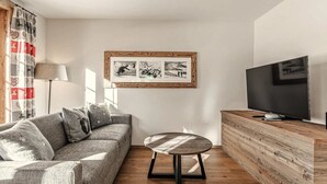 Een moderne woonkamer met een bank, een ronde tafel, een televisie en een lijst met een afbeelding aan de muur.