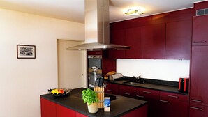 A modern kitchen with red cabinetry, a central island, and a stainless steel range hood. - Valletta Appartement/Fewo, Dusche oder Bad, WC, 6-Bettwohnung by Interhome (Arosa)