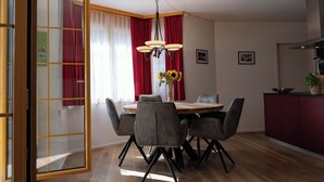A dining area with a table, chairs, a chandelier, and a kitchen in the background. - Valletta Appartement/Fewo, Dusche oder Bad, WC, 6-Bettwohnung by Interhome (Arosa)