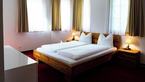 A hotel room with a wooden bed, two bedside lamps, and a window with curtains. - Valletta Appartement/Fewo, Dusche oder Bad, WC, 6-Bettwohnung by Interhome (Arosa)
