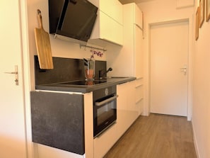 A compact kitchen with a built-in oven, a countertop, and a hanging pot rack. - ArosaFlair Studio, Dusche, WC, Balkon by Interhome (Arosa)