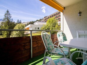 Ein Balkon mit Tisch und Stühlen, ein Holzzaun und Blick auf Gebäude und Bäume.
