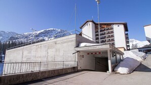 A concrete building with a parking garage entrance, a snow-covered mountain in the background, and a clear blue sky. - Rothornblick 19 Appartement/Fewo, Bad, WC, 3-Bettwohnung Rothornblick 19 by Interhome (Arosa)