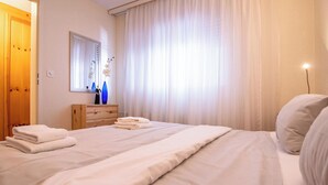 A neatly made bed with folded towels, a wooden dresser, a mirror, and a window with sheer curtains. - Rothornblick 19 Appartement/Fewo, Bad, WC, 3-Bettwohnung Rothornblick 19 by Interhome (Arosa)