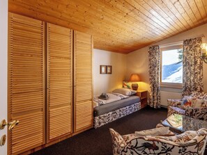 A room with a bed, a sofa, a window with curtains, a lamp, and wooden paneling on the walls and ceiling. - Haus Duranna 7 Appartement/Fewo, Bad, WC, 4-Bettwohnung by Interhome (Arosa)