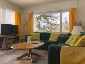 Ett vardagsrum med en tv, en soffa, ett soffbord och ett fönster med gardiner.