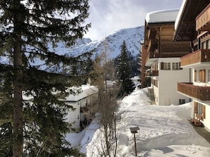 Paisaje nevado de una montaña con un edificio que tiene balcones y un techo cubierto de nieve.