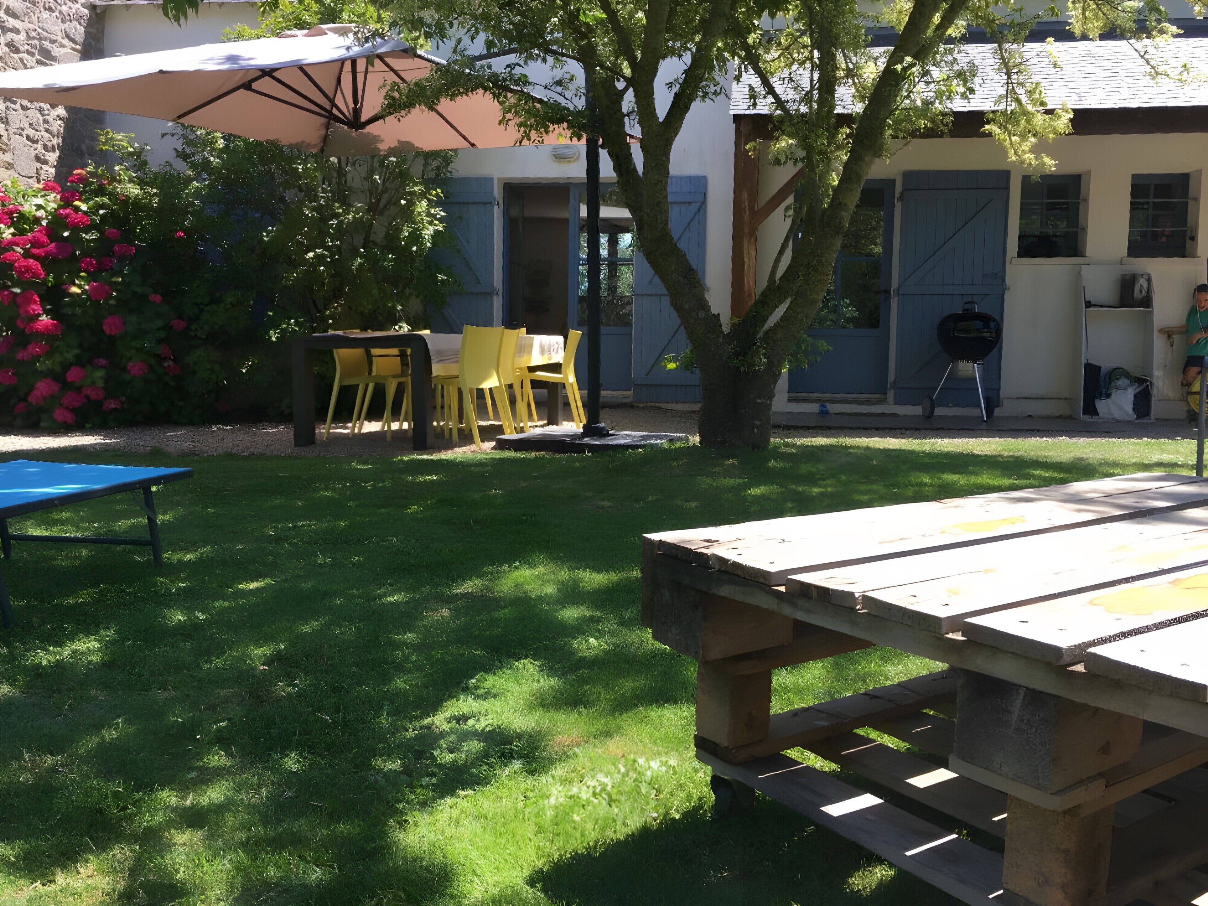 Ein Garten mit einem Holztisch, gelben Stühlen und einem Grill.