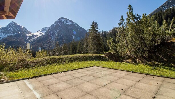 Ein gepflasterter Außenbereich mit Blick auf schneebedeckte Berge und dichten Wald.