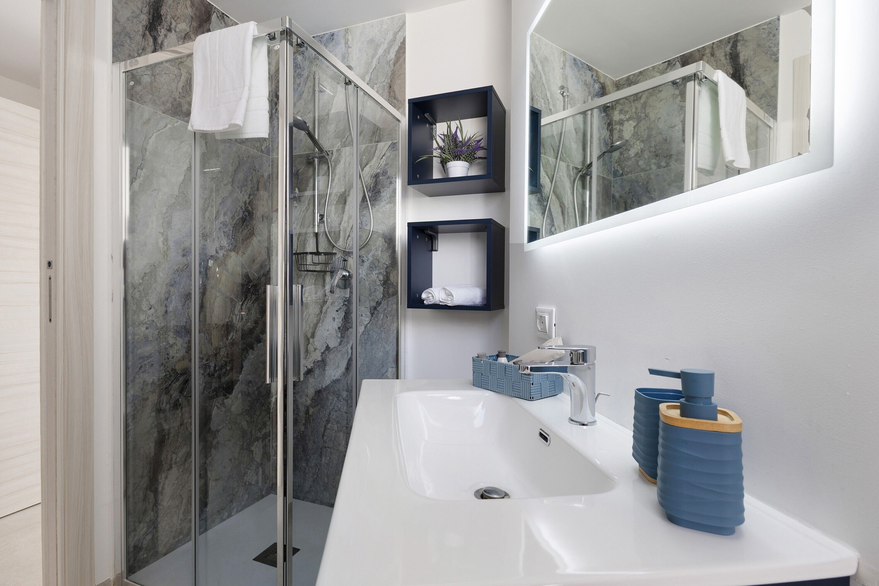 A modern bathroom with a glass shower enclosure, a white sink, and a mirror.