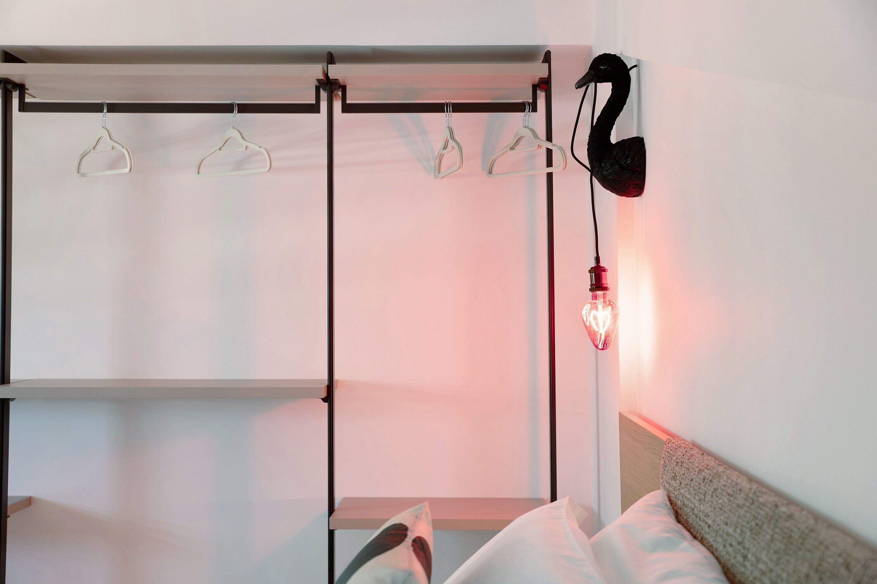 En seng med gavl, en vægmonteret lampe og et tøjstativ med knager.