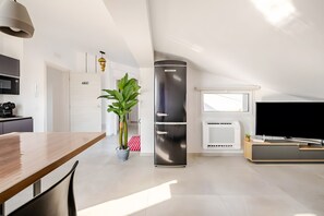Una cocina moderna con horno empotrado, refrigerador y comedor con mesa y sillas de madera.