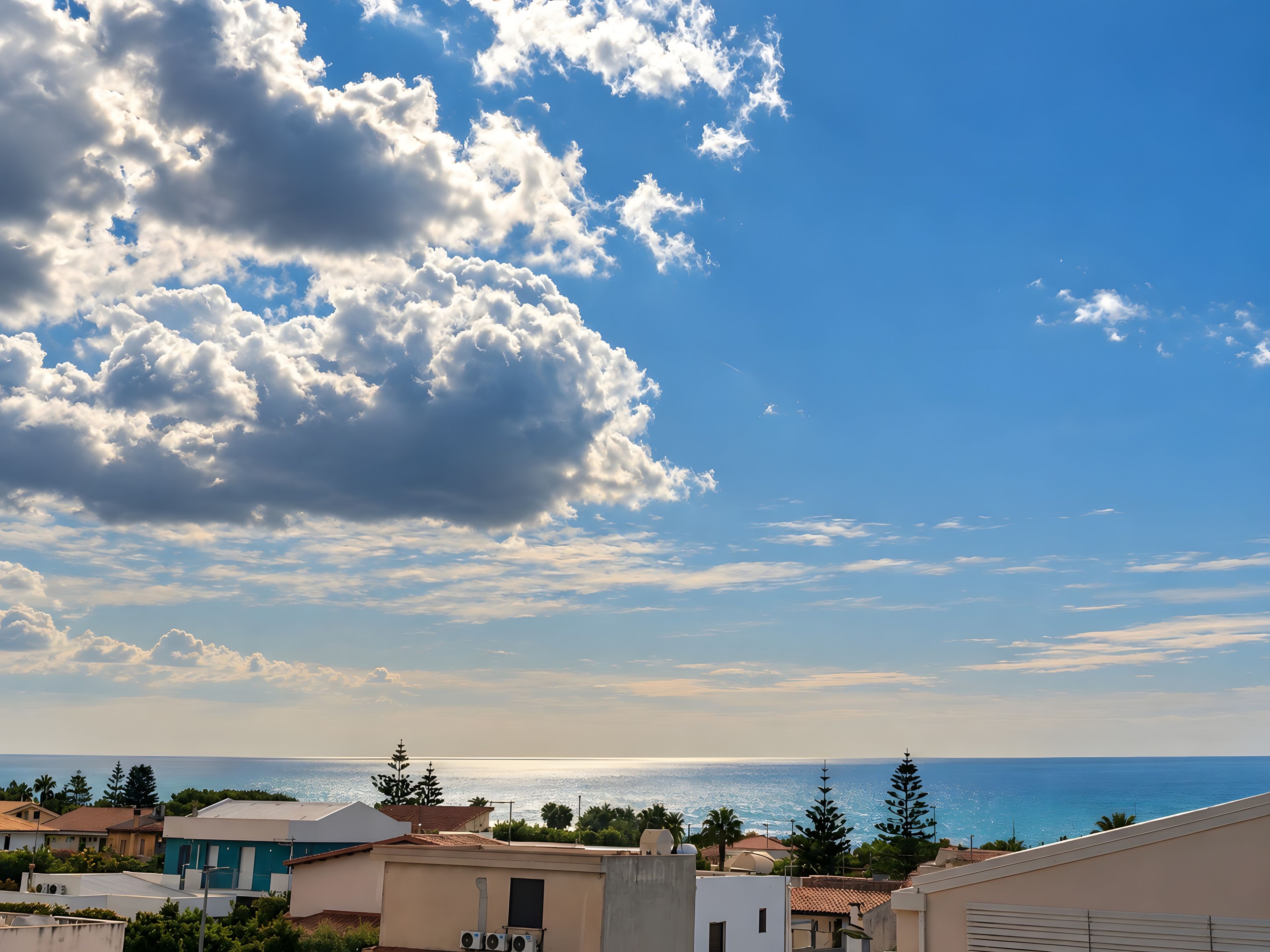 A coastal residential area with houses, a clear sky, and the sea in the background.