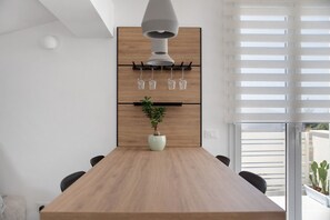 A modern dining area with a wooden table, chairs, a potted plant, and a wine rack with glasses. - Giordano Luxury penthouse Sea View private terrace and spa (Santa Maria del Focallo)