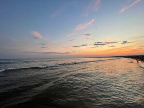 Escena de playa con olas y un atardecer.