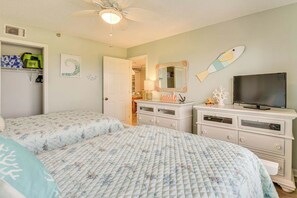 Ein Schlafzimmer mit zwei Betten, einem Schminktisch, einem Fernseher und einem Deckenventilator.