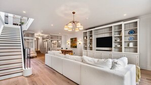 Ein modernes Wohnzimmer mit einem weißen Sofa, einer Treppe, einem Essbereich und integrierten Regalen mit Dekorationsobjekten.