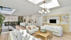 Ein modernes Wohnzimmer mit einer Couch, einem Couchtisch und einem Fernseher. Es gibt einen Essbereich mit Tisch und Stühlen, und im Hintergrund eine Küche.