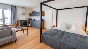 Een moderne hotelkamer met een bed, een slaapbank, een tafeltje, een kitchenette en een raam.