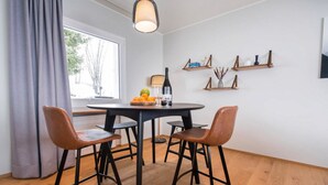 Een eetgedeelte met een ronde tafel, vier stoelen, een hanglamp en houten planken met decoratieve objecten.