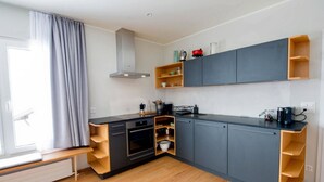 Een moderne keuken met grijze kastjes, houten planken, een ingebouwde oven en een raam met grijze gordijnen.