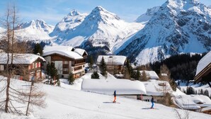 Een bergresort bedekt met sneeuw, met skipistes, houten gebouwen en een heldere lucht.
