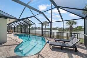A covered outdoor swimming pool with lounge chairs and a view of a lake. - Murex Home – Luxury Sanibel Island Pool Home | Lake Views | Walk to Beach (Sanibel)