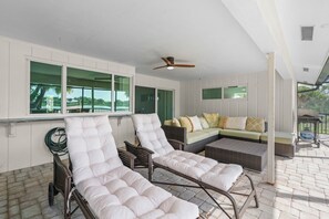 Eine sonnendurchflutete Terrasse mit zwei Liegestühlen, einer Couch und einem Deckenventilator.