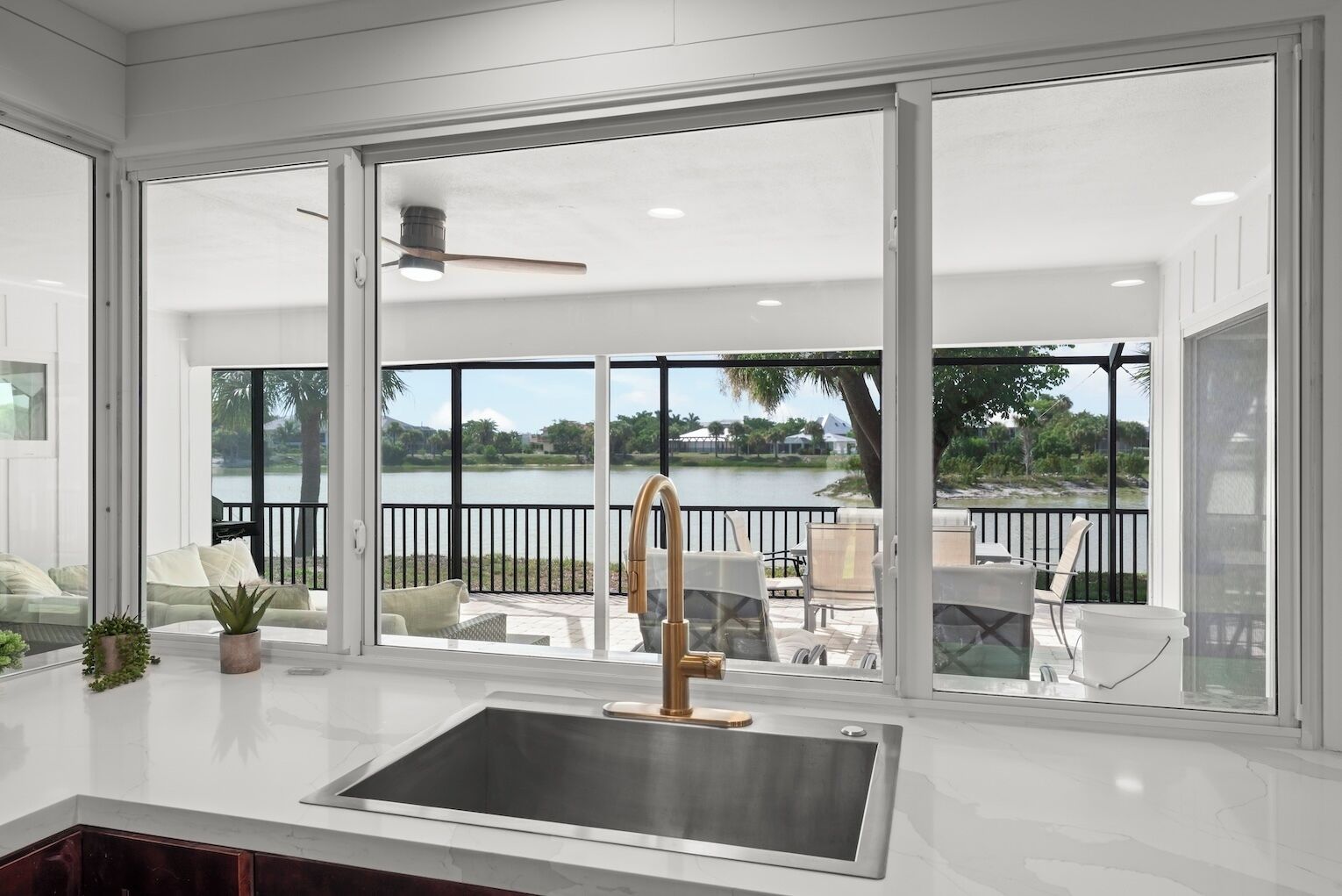 A modern kitchen with a large window, a stainless steel sink, and a view of a lake and outdoor seating area.