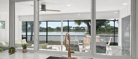 A modern kitchen with a large window, a stainless steel sink, and a view of a lake and outdoor seating area.