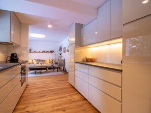 A modern kitchen with white cabinetry, a wooden floor, and a dining area with a sofa and table. - Bella Riva by Arosa Holiday Appartement/Fewo, Dusche oder Bad, WC, 5-Bettwohnung by Interhome (Arosa)