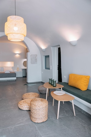 A modern interior with a sofa, a table with vases, wicker ottomans, and a hanging light fixture. - Agave Cave Studios (Santorini)