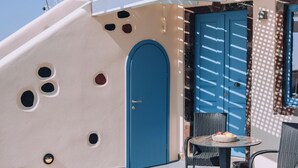 Een gebouw met een blauwe deur, een tafeltje met stoelen en een bloempot.