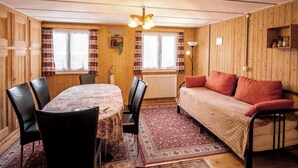 Ein gemütliches Zimmer mit Holzvertäfelung, einem Esstisch mit Stühlen, einer Couch und einer Heizung.