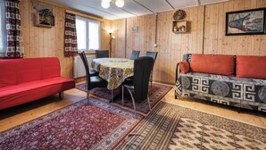 Ein gemütlicher Raum mit einem roten Sofa, einem gemusterten Sofa, einem Esstisch mit Stühlen und einer Holzwand mit einer Uhr und einem gerahmten Bild.