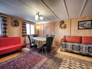A cozy room with a red sofa, a patterned sofa, a dining table with chairs, and a wooden wall with a clock and a framed picture. - Nühus 1. OG Appartement/Fewo, Bad, WC, 6-Bettwohnung by Interhome (Arosa)