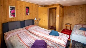 Ein Zimmer mit Holzwandverkleidung, zwei Betten, einer Tür zu einem anderen Raum und einem kleinen Tisch mit Lampe.