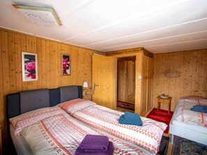 A wooden-paneled room with two beds, a door leading to another room, and a small table with a lamp. - Nühus 1. OG Appartement/Fewo, Bad, WC, 6-Bettwohnung by Interhome (Arosa)