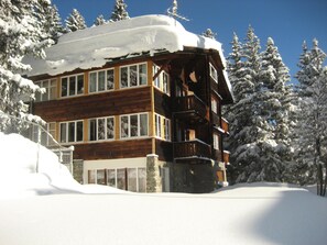 Eine mehrstöckige Holzlodge mit großen Fenstern, umgeben von schneebedeckten Bäumen.
