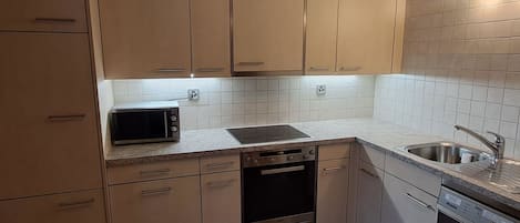 Uma cozinha com armários bege, micro-ondas, lava-louças e pia.