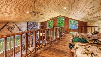 A cabin with a wooden interior, a stone fireplace, and a balcony with a view of the outdoors.