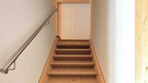 A wooden staircase with a handrail, leading to a landing with a light switch. - Erzhornblick Appartement/Fewo, Dusche und Bad, WC, 3 Schlafräume by Interhome (Arosa)