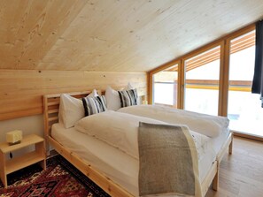 Ein Schlafzimmer mit Holzboden, einem großen Bett mit weißer Bettwäsche, einem Nachttisch und einem Fenster mit Blick.