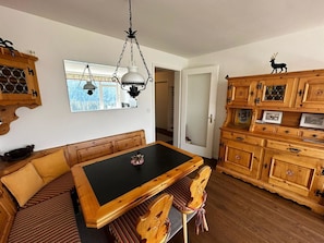 Ein Essbereich mit Holztisch und Bank, einer Kristallleuchter und Holzschränken mit Glastüren.
